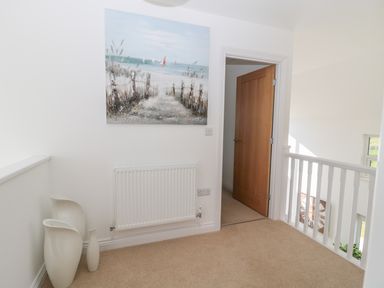 A hallway with beige carpet a wooden door white radiator three white vases and a painting of a beach at Waterside in Beadnell