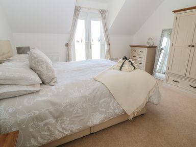 A bedroom with a bed with patterned bedding folded towels on the bed a chest of drawers a mirror and a wardrobe at Waterside in Beadnell