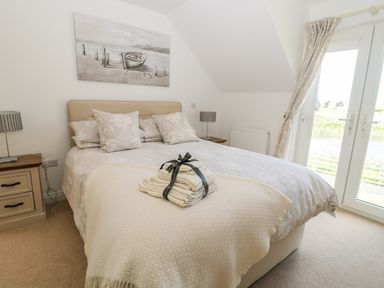 A bedroom with a bed with pillows and folded towels on it next to windows with curtains at Waterside in Beadnell