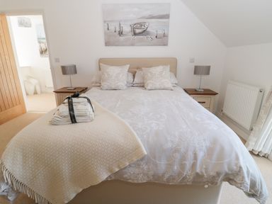 A bedroom with a double bed two bedside tables with lamps and a painting above the bed at Waterside in Beadnell