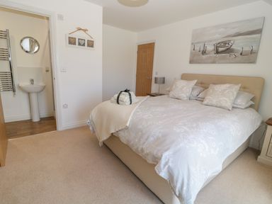 A bedroom with a double bed pillows a bedside table lamp a wooden door and an ensuite bathroom with a sink at Waterside in Beadnell