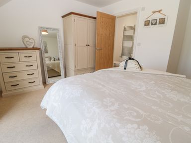 A bedroom with a bed, wardrobe, chest of drawers, mirror, and an open door leading to a bathroom at Waterside in Beadnell