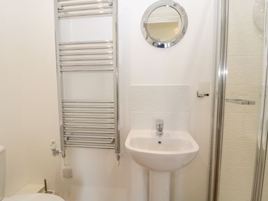 A bathroom with a sink a round mirror a heated towel rail and a glass shower enclosure at Waterside Beadnell