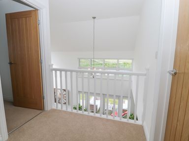 A landing with beige carpet and two wooden doors overlooking a living area with a large clock and windows at Waterside in Beadnell