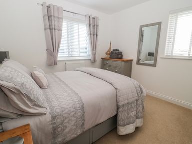 A bedroom with a bed covered with a patterned duvet and pillows a chest of drawers with folded towels and a decorative sailboat and a wall mirror at Waterside in Beadnell
