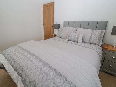 A bedroom with a bed featuring gray and white bedding two bedside tables with lamps and a wooden door at Waterside in Beadnell