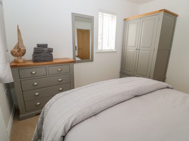 A bedroom with a bed a dresser with folded towels a wardrobe and a wall mirror at Waterside in Beadnell