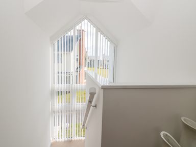A stairway with a handrail next to a large triangular window with vertical blinds at Waterside in Beadnell