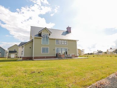 A detached house with patio furniture on a grassy lawn in a residential area at Waterside in Beadnell