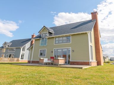 A garden with outdoor seating area and two houses under a blue sky at Waterside in Beadnell