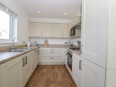 A kitchen with white cabinets wooden countertops a sink stove oven microwave and wooden floor at Waterside in Beadnell