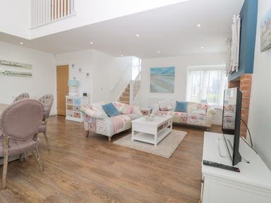 A living room with two patterned sofas a white coffee table a television and dining chairs at Waterside in Beadnell