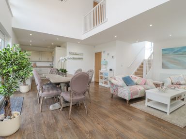 A dining area with a table and chairs next to a living room with sofas a coffee table and a staircase at Waterside in Beadnell