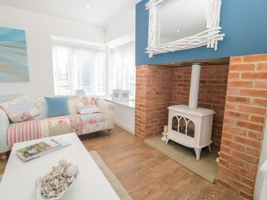 A living room with a patchwork sofa white wood stove in a red brick fireplace and a white coffee table at Waterside in Beadnell