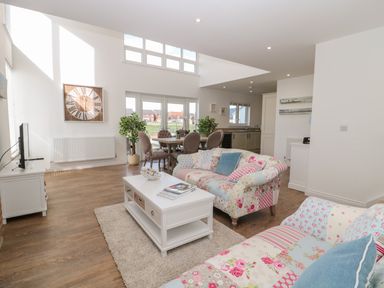 A living room with floral sofas white coffee table and dining area with round table and chairs at Waterside in Beadnell