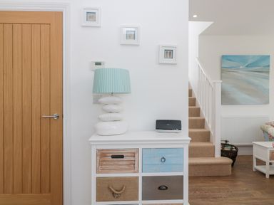 A white cabinet with drawers and a blue lamp on top next to a wooden door and beige stairs at Waterside in Beadnell