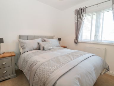 A bedroom with a bed with gray bedding gray curtains and bedside tables with lamps at Waterside in Beadnell