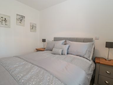 A bedroom with a grey upholstered bed and grey bedding with two bedside tables and lamps at Waterside in Beadnell