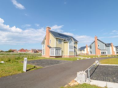 A residential street with detached houses and driveways under a blue sky at Waterside in Beadnell