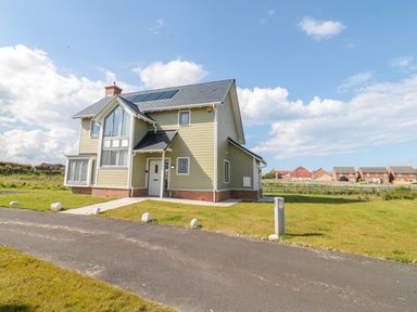 A detached two-story house with a front lawn and solar panels on the roof at Waterside in Beadnell