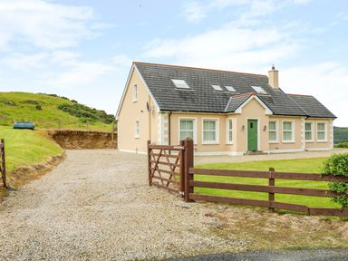 A detached house with a green front door surrounded by a gravel driveway and a wooden gate at Croghan in Portsalon