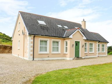 A beige house with a green door and multiple windows surrounded by gravel and grass at Croghan in Portsalon