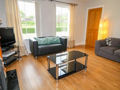 A living room with two sofas a glass coffee table a television and a floor lamp at Croghan in Portsalon