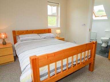 A bedroom with a wooden bed and striped bedding and two bedside tables with lamps next to a bathroom with a toilet at Croghan in Portsalon