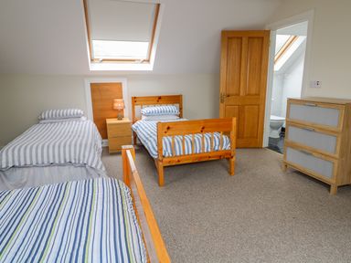 A bedroom with three single beds two with striped bedding a wooden dresser and an open door to a bathroom at Croghan in Portsalon