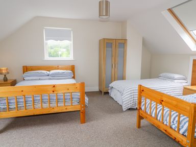 A bedroom with three wooden beds a wooden wardrobe and two windows at Croghan in Portsalon