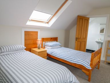 A bedroom with two single beds a bedside table with a lamp a skylight window and an open door leading to a bathroom at Croghan in Portsalon