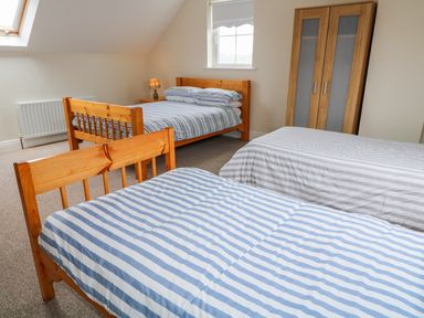 A bedroom with three beds two with striped bed covers a wooden wardrobe and a small lamp on a bedside table at Croghan in Portsalon