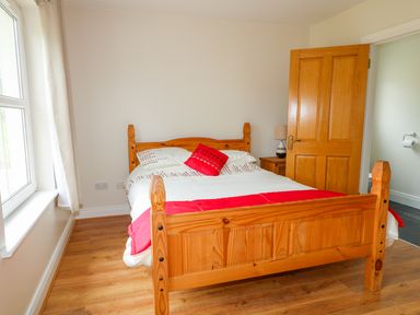 A bedroom with a wooden bed with white and red bedding a nightstand with a lamp and a partially open wooden door at Croghan in Portsalon