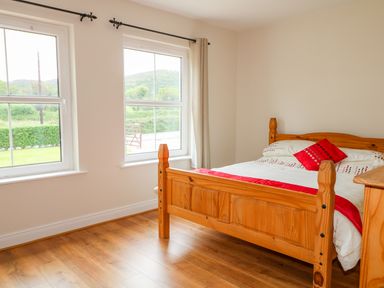 A bedroom with a wooden bed with white and red bedding and two windows showing greenery outside at Croghan in Portsalon