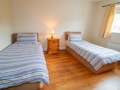 A bedroom with two single beds with striped bedding and a wooden nightstand with a lamp in between at Croghan Portsalon