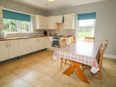 A kitchen with cream cabinets a wooden dining table with chairs and windows with blue blinds at Croghan in Portsalon