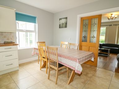 A dining area with a wooden table covered with a tablecloth and six wooden chairs near a window and wooden door at Croghan in Portsalon