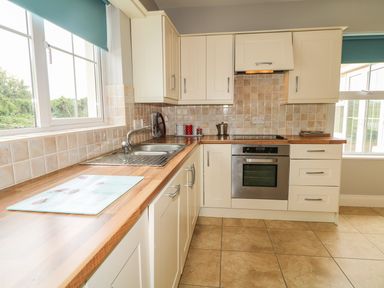 A kitchen with cream cabinets wooden countertops a stainless steel oven sink and tiled floor at Croghan in Portsalon