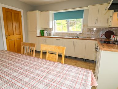A kitchen with cabinets a wooden door a table with a plaid tablecloth and wooden chairs at Croghan in Portsalon