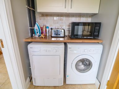A laundry area with a washing machine and dryer under a wooden countertop with a microwave oven toaster and iron on top at Croghan in Portsalon
