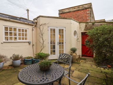 A small courtyard with a metal table and chairs several potted plants and a red door at 20A St Hilda's Whitby