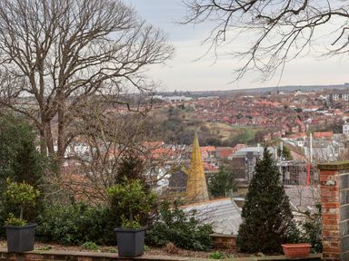 A view of houses and buildings with trees in the foreground and a church spire at 20A St Hildas in Whitby