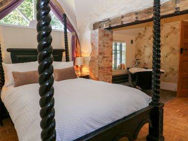 A bedroom with a black four poster bed white bedding and adjacent bathroom with black clawfoot tub at The Hemmel in Faringdon