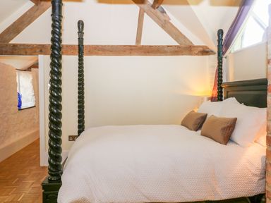 A bedroom with a four poster bed white bedding two brown pillows and wooden beams at The Hemmel in Faringdon