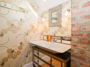 A bathroom sink with a mirror above it and floral wallpaper next to a brick wall at The Hemmel in Faringdon