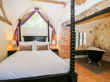 A bedroom with a four-poster bed and a black clawfoot bathtub near a window at The Hemmel in Faringdon