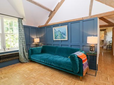 A room with a teal sofa blue paneled walls wooden beams two lamps a window with patterned curtains and a parquet floor at The Hemmel in Faringdon