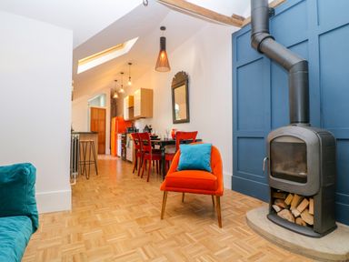 A kitchen and dining area with a wood-burning stove and orange chair at The Hemmel in Faringdon
