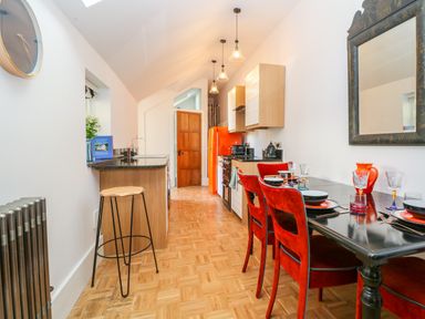 A kitchen with a wooden floor a black dining table with red chairs and an orange refrigerator at The Hemmel in Faringdon