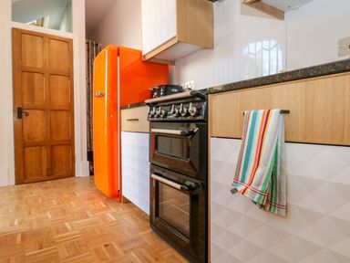 A kitchen with a black oven orange fridge wooden cabinets and a striped towel at The Hemmel in Faringdon